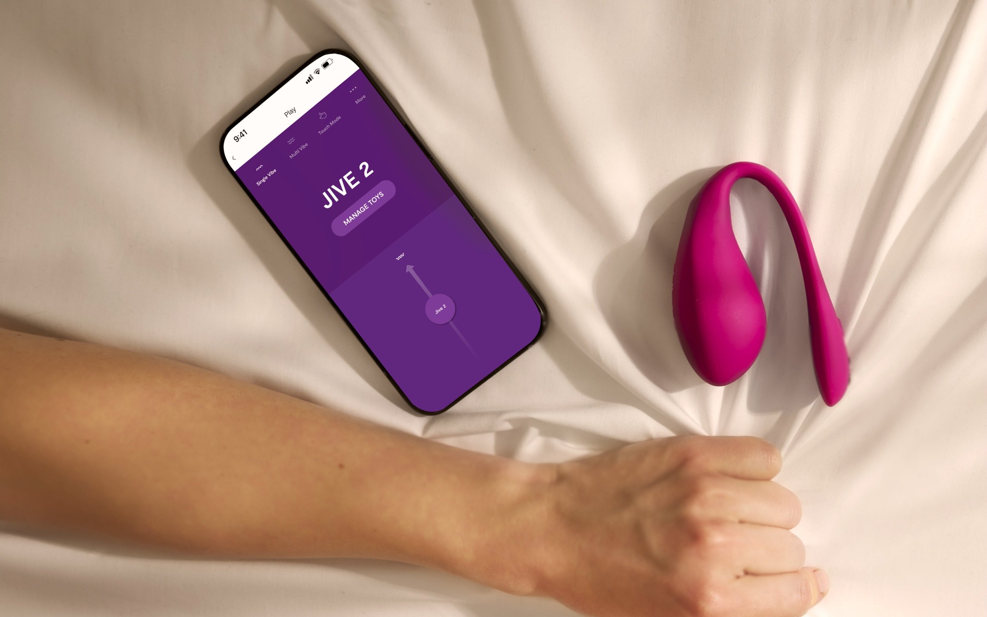 We-Vibe Jive 2 紫色跳蛋與手機並置於織紋布面,螢幕顯示 We-Vibe App 控制介面,自然光影